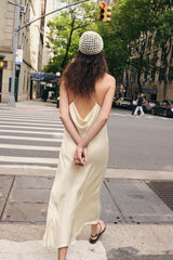 Woman in a cream-colored dress with a backless design walking on a city street.