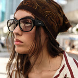 Woman wearing a brown beanie and striped shirt with glasses, outdoors.