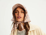 Woman wearing a beige jacket, plaid bonnet, and gray shirt on a white background