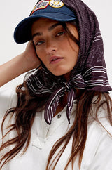 Woman wearing a white shirt, red shorts, and a blue cap with a patterned headscarf on a white background