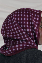 Person wearing a purple checkered headscarf against a white background