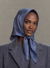 Woman wearing a blue headscarf and gray coat against a beige background