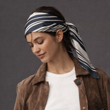 Woman wearing a brown jacket and white shirt with a striped headscarf on a gray background