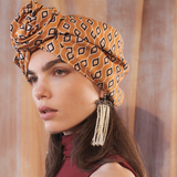 Woman wearing a patterned headscarf with tassels against a soft, neutral background