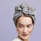 Woman wearing a gray headscarf against a light purple background