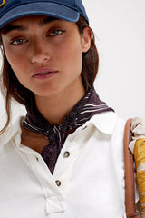 Woman wearing a blue cap, white shirt, and patterned scarf with a white background
