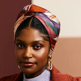Woman wearing a colorful headscarf, red jacket, and gray sweater against a neutral background