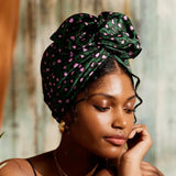 Woman wearing a green headscarf with pink patterns, posing thoughtfully.