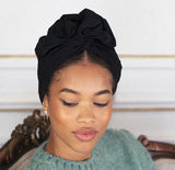 Woman wearing a black headscarf and green sweater against a neutral background