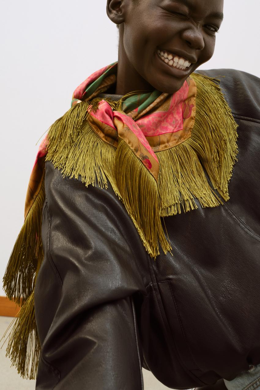 Person wearing a dark leather jacket with a colorful fringed scarf