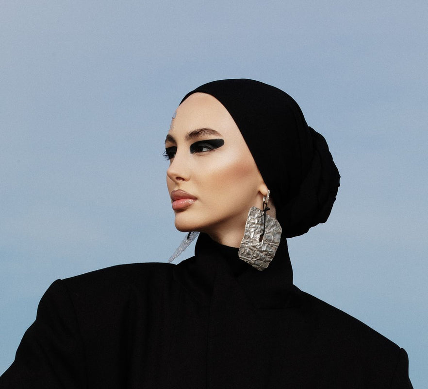 Woman wearing a black hijab and black outfit against a light blue background
