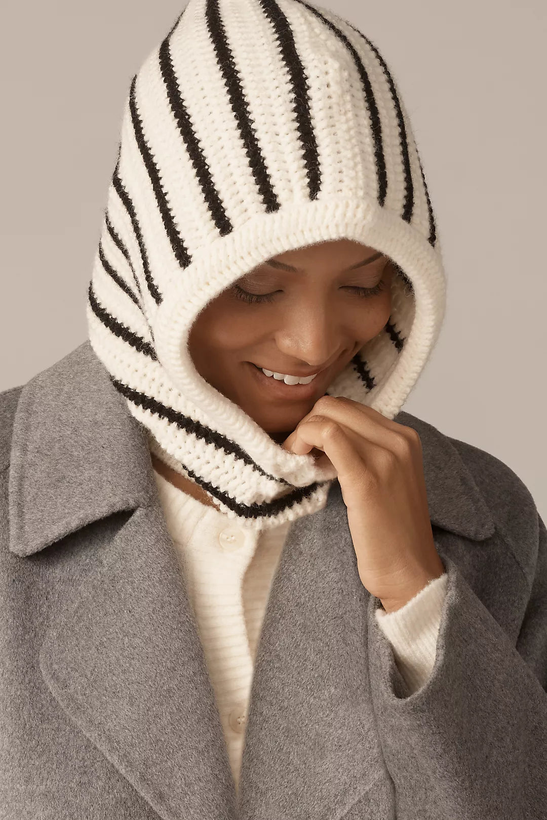 Person wearing a gray coat and a striped knitted hood against a neutral background