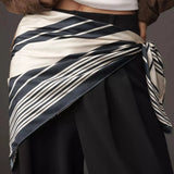 Person wearing a white top, black pants, and a striped sash against a gray background