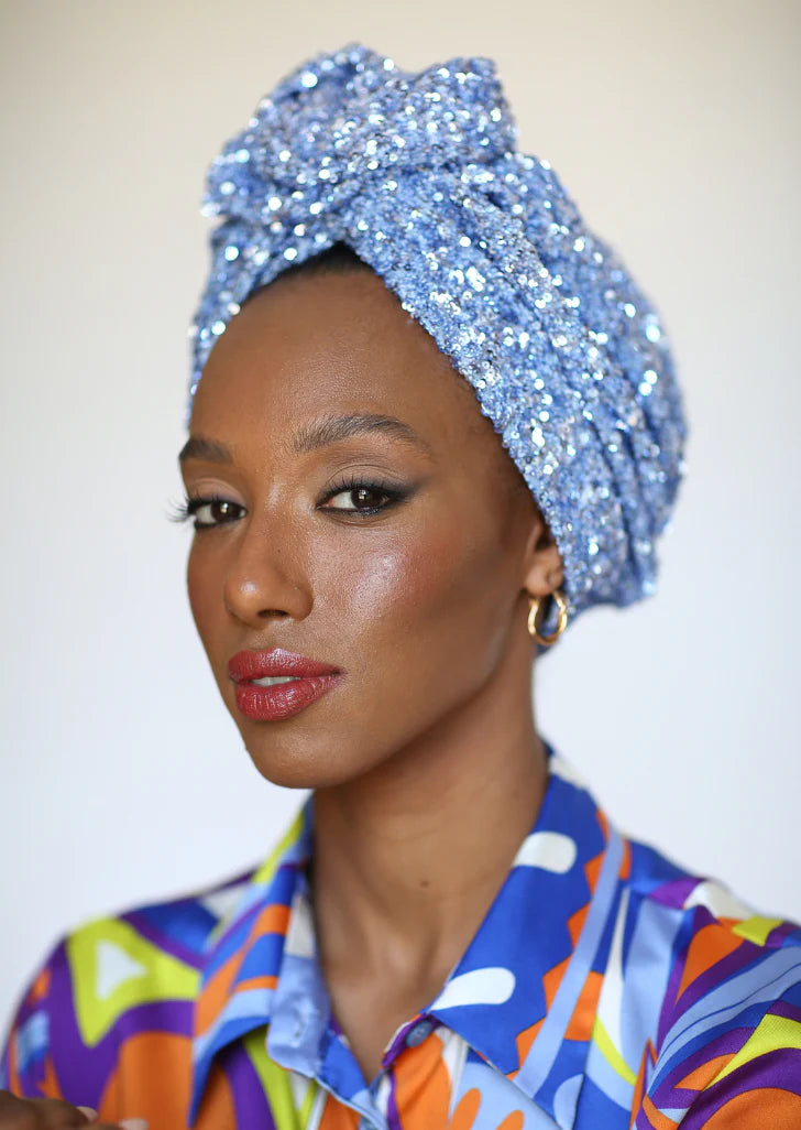 Woman wearing a colorful patterned shirt and a blue sequin headwrap against a plain background