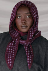 Person wearing a dark gray coat and a purple checkered headscarf against a plain background