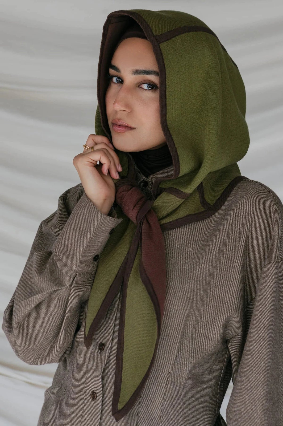 Woman wearing a green headscarf with brown accents against a plain background