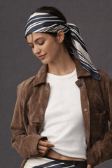 Woman wearing a brown jacket and white shirt with a striped headscarf on a gray background