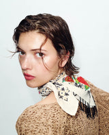 Woman wearing a patterned scarf and beige sweater against a white background