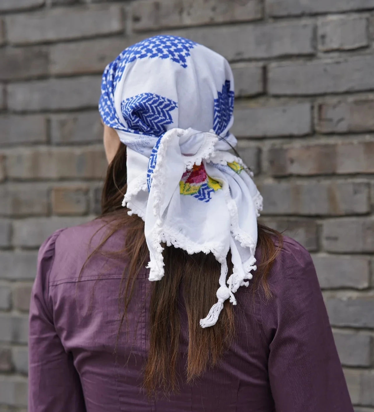 Person wearing a colorful headscarf with a brick wall background