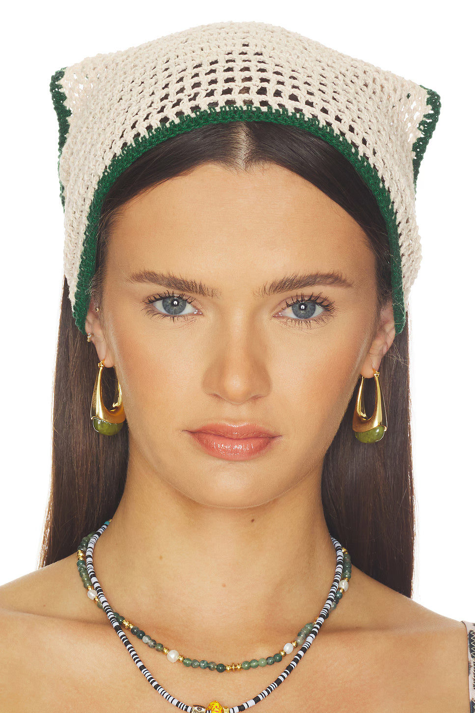 Woman wearing a crocheted hat with green trim and gold hoop earrings.