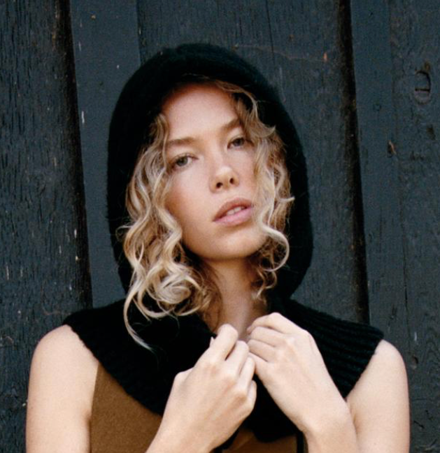 Woman wearing a black hooded garment against a dark wooden background