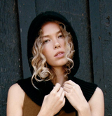 Woman wearing a black hooded garment against a dark wooden background