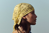 Woman wearing a yellow headscarf and denim jacket against a clear sky.