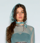 Person wearing a sheer teal outfit with a hood against a light gray background