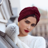 Woman wearing a white knitted sweater and red headscarf, sitting in a car.
