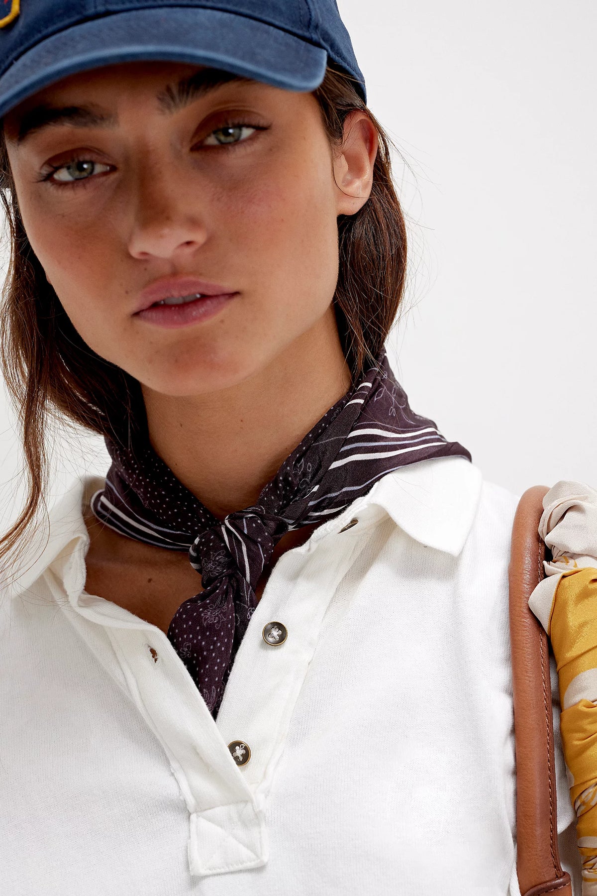 Woman wearing a blue cap, white shirt, and patterned scarf with a white background