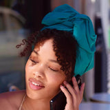 Woman with teal headscarf talking on a phone in an outdoor setting