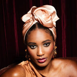 Woman wearing a pink headscarf and gold dress against a dark background
