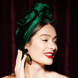 Woman wearing a green headscarf and gold earrings against a dark background