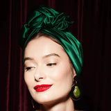 Woman wearing a green headscarf and red lipstick against a dark background