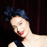 Woman with blue hair and red lipstick wearing a black dress against a dark background