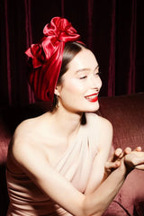 Woman with a large red bow in her hair against a dark background