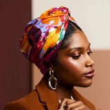 Woman wearing a colorful headscarf and brown blazer against a beige background