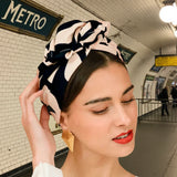 Woman wearing a black and beige patterned headscarf with a pink background