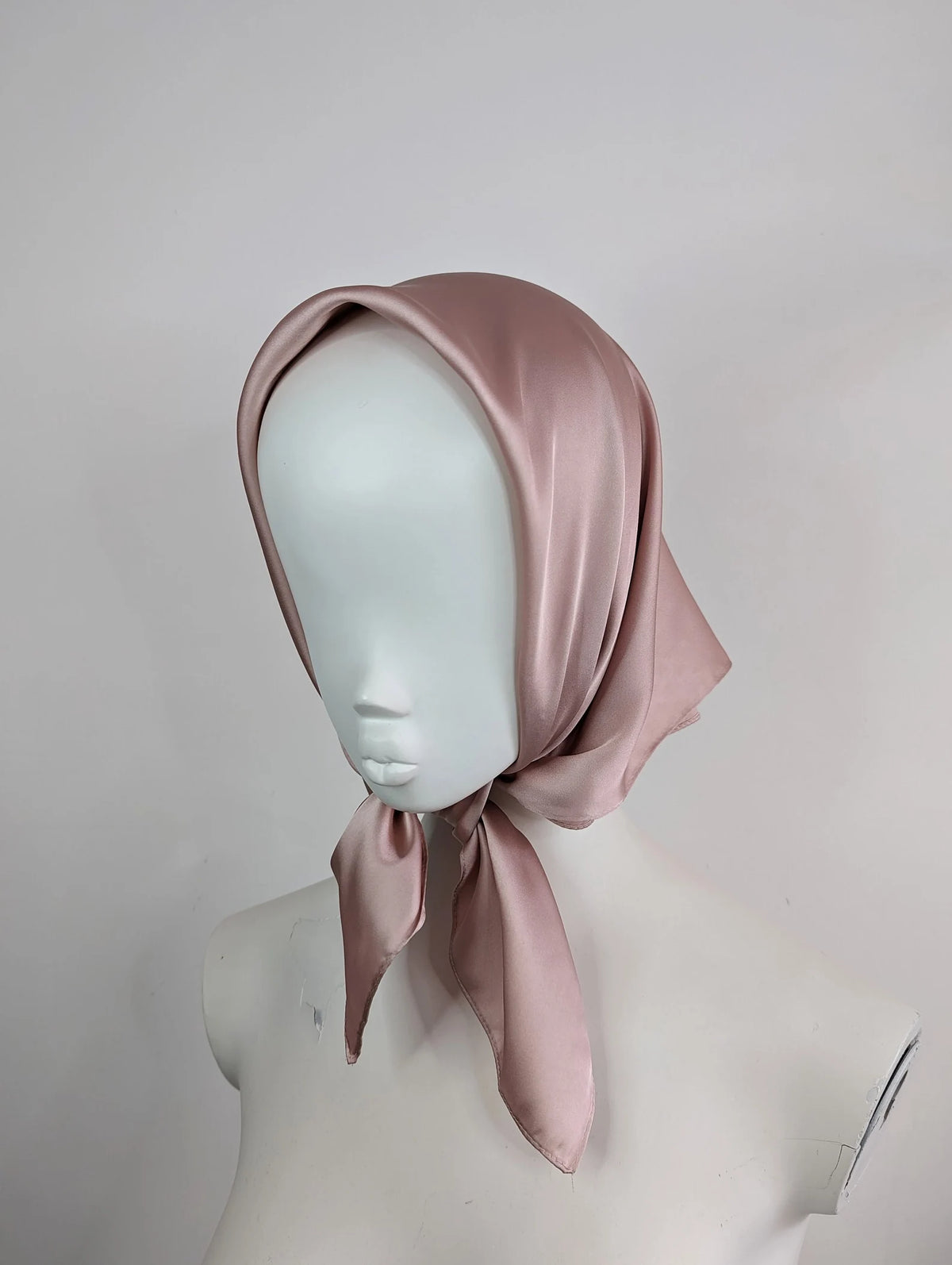 Mannequin head wearing a light pink satin headscarf against a plain background