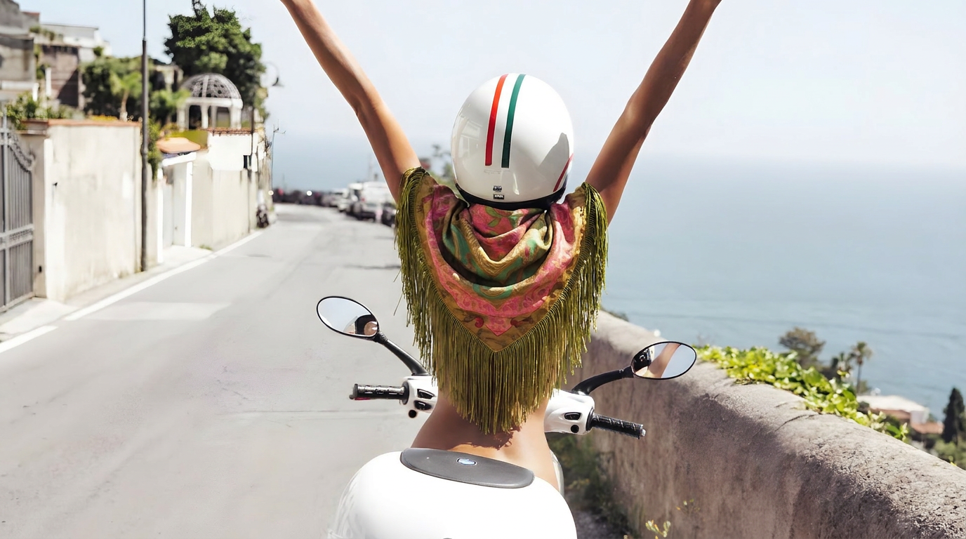 Person on a scooter with arms raised by the sea